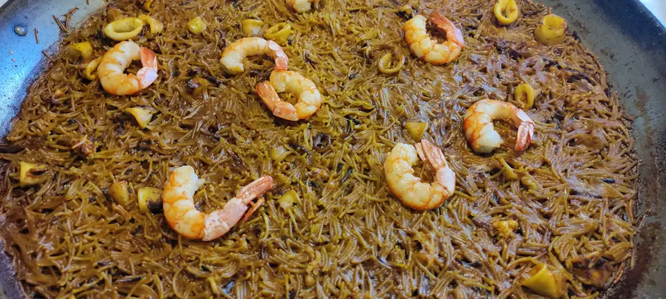 Fideuà dorée dans sa poêle, garnie de fruits de mer