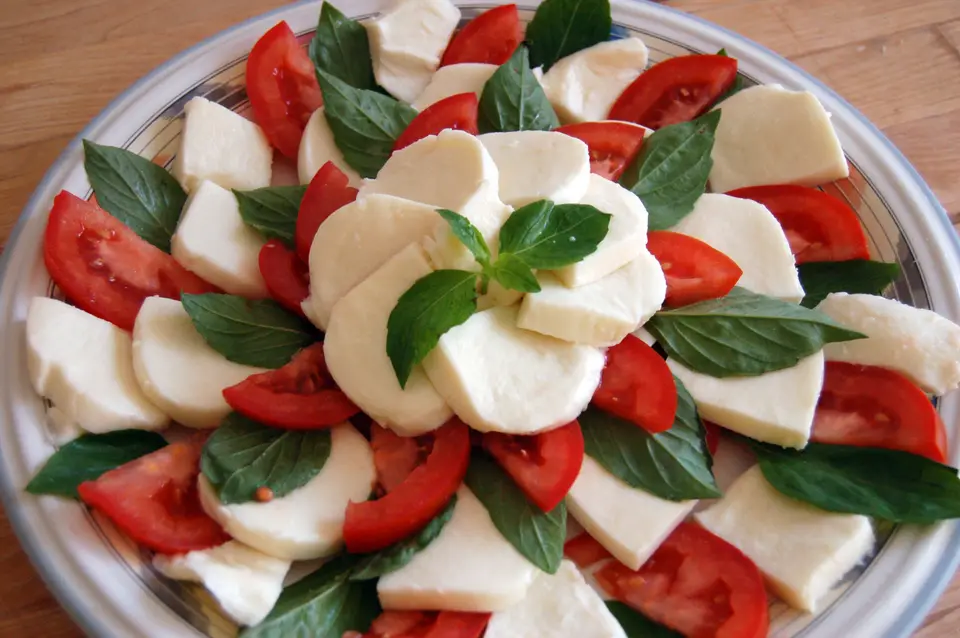 Salade caprese : tranches de tomate et de mozzarella alternées, feuilles de basilic