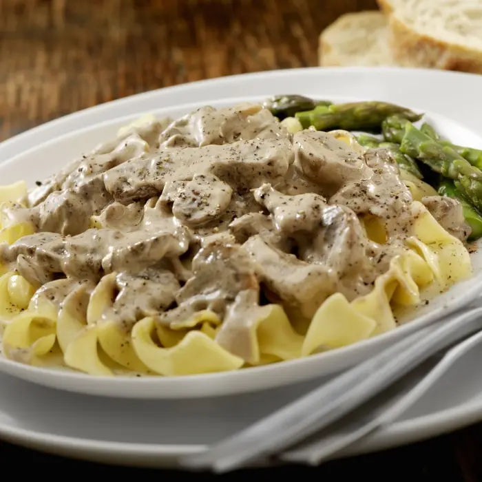 Bœuf Stroganoff crémeux aux champignons sur des pâtes, quelques asperges à côté