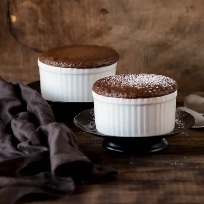 Deux soufflés au chocolat montés dans leurs ramequins blancs, saupoudrés de sucre glace