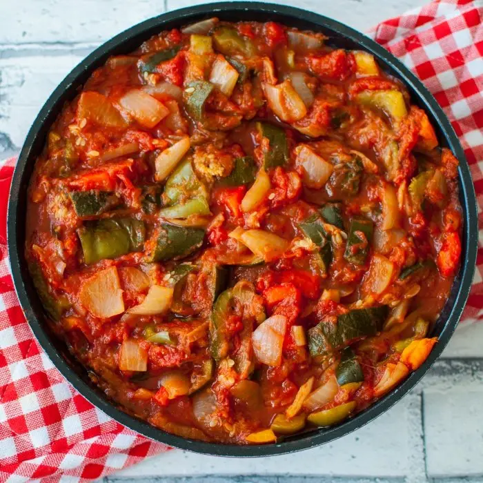 Ratatouille aux légumes confits dans une sauteuse noire, sur une nappe à carreaux