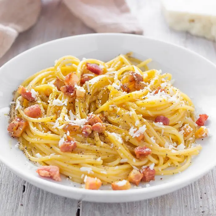 Spaghetti à la carbonara, dés de pancetta et fromage râpé, dans une assiette blanche