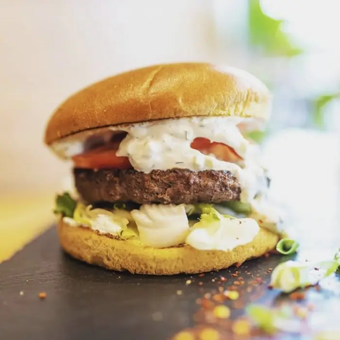 Burger d'agneau garni de tzatziki et de tomate, sur fond clair
