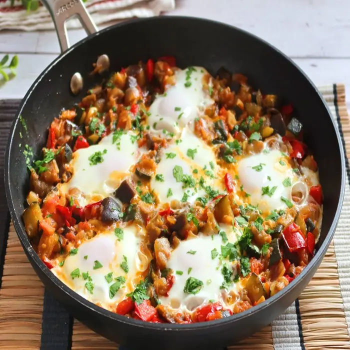 Pisto de légumes et œufs cuits dans la sauce, dans une poêle noire, persil ciselé