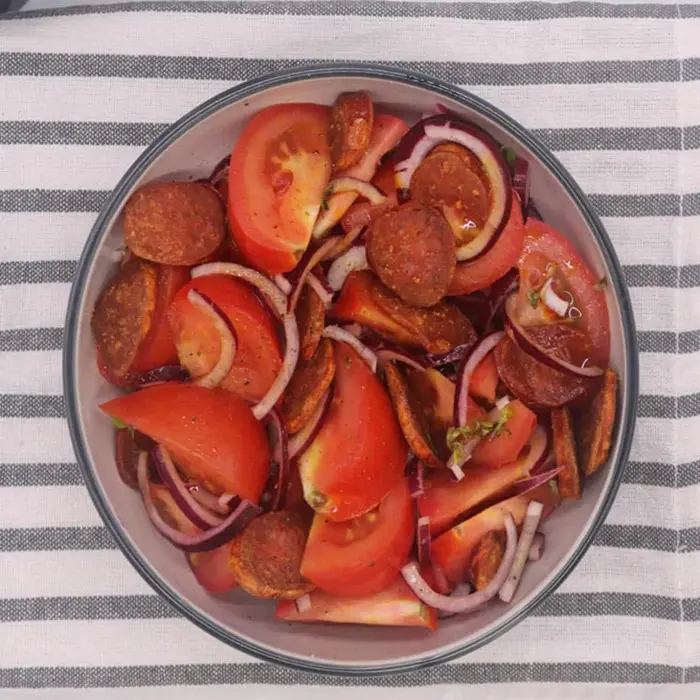 Quartiers de tomate, oignon rouge et rondelles de chorizo dans une assiette